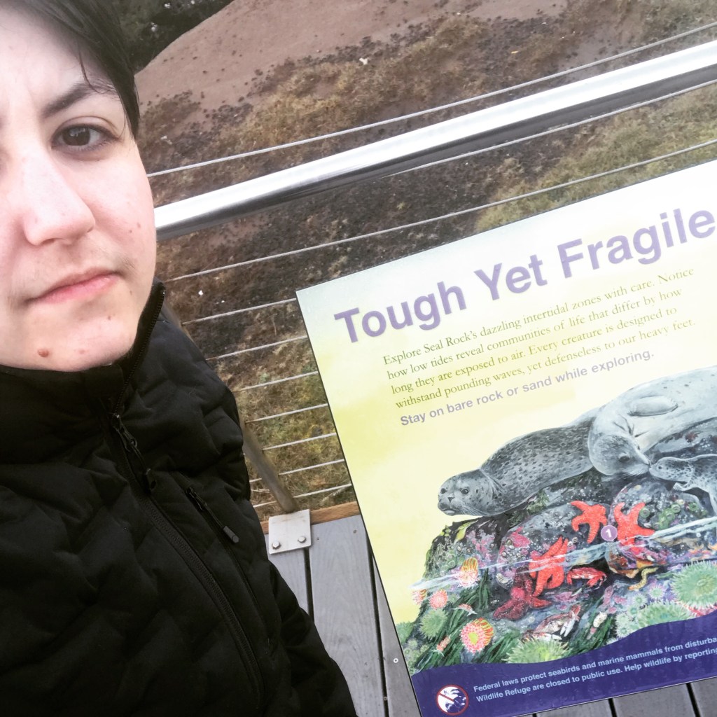 a selfie of R.J. Tenace (Robin) angled to include the text from an infographic display at the beach that says "Tough Yet Fragile"
